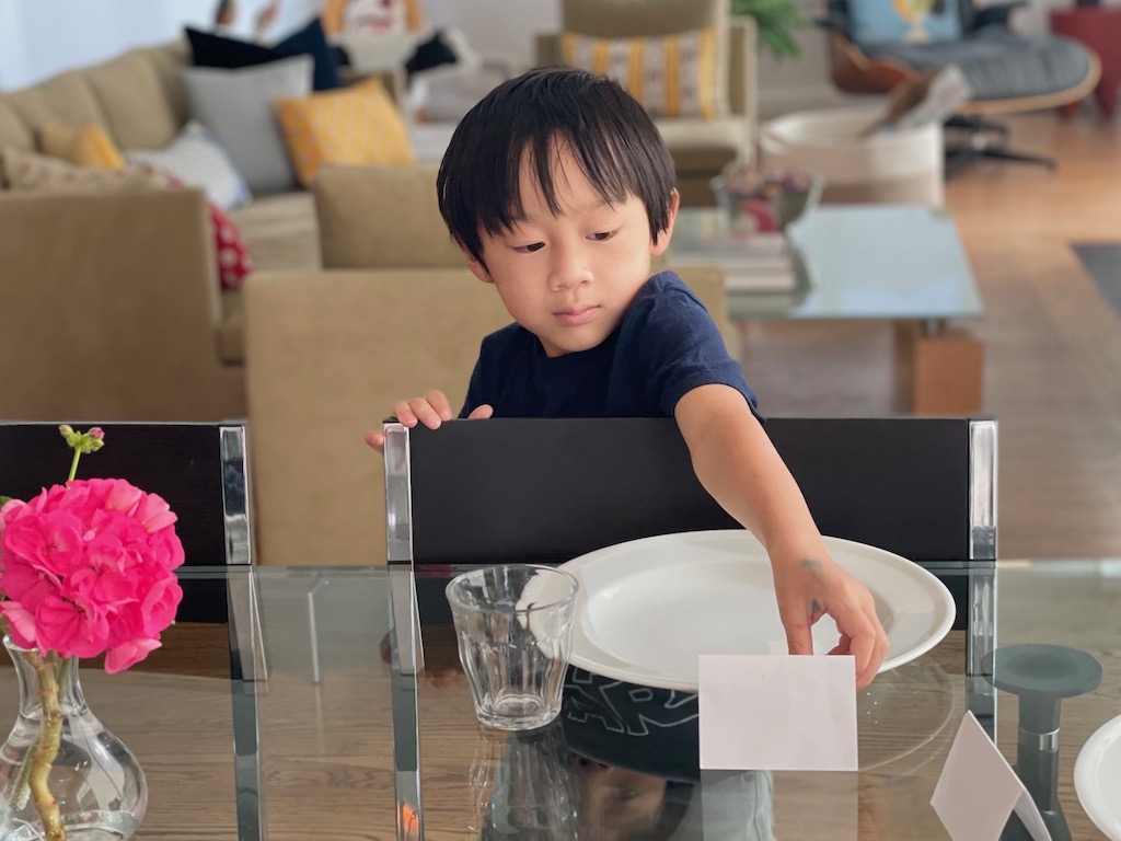Younger boy sets the table, adding a place card.
