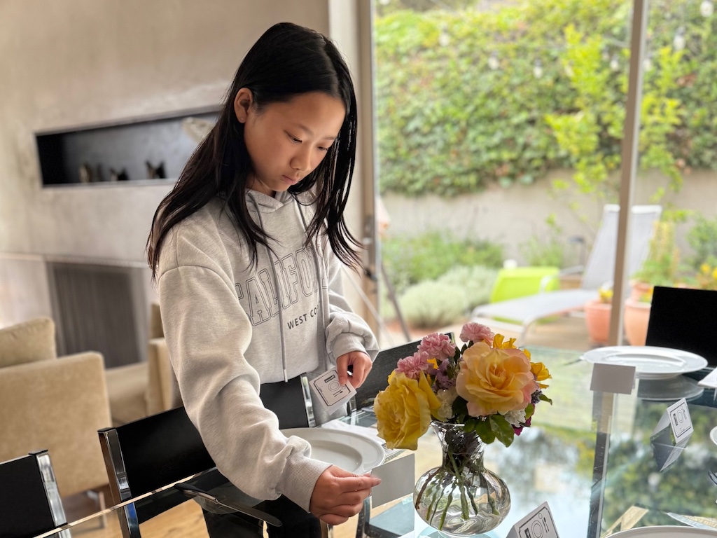 Older child sets the table for the weekly family dinner, adding a place card at each place setting.