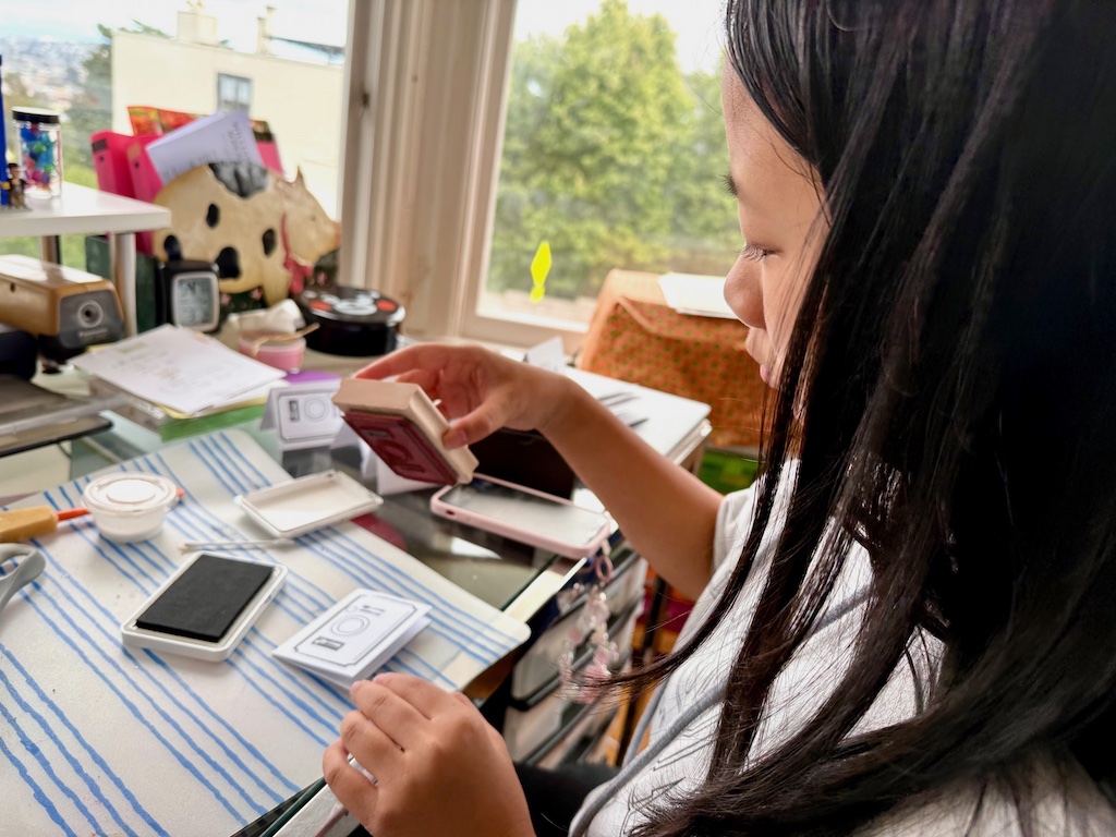 Older child stamps design for place cards using a wooden stamp; next she'll write the names of the diners on each place card.