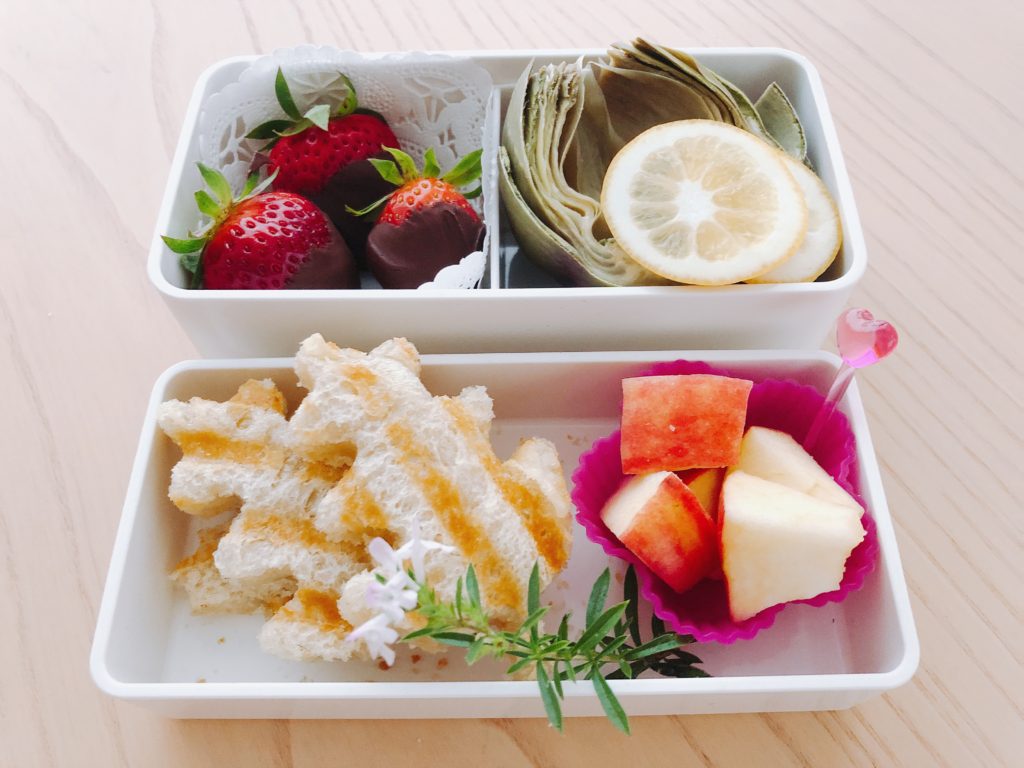 Grilled cheese sandwiches cut in leaf shapes, apple wedges, artichoke half and chocolate-dipped strawberries fill this bento box.
