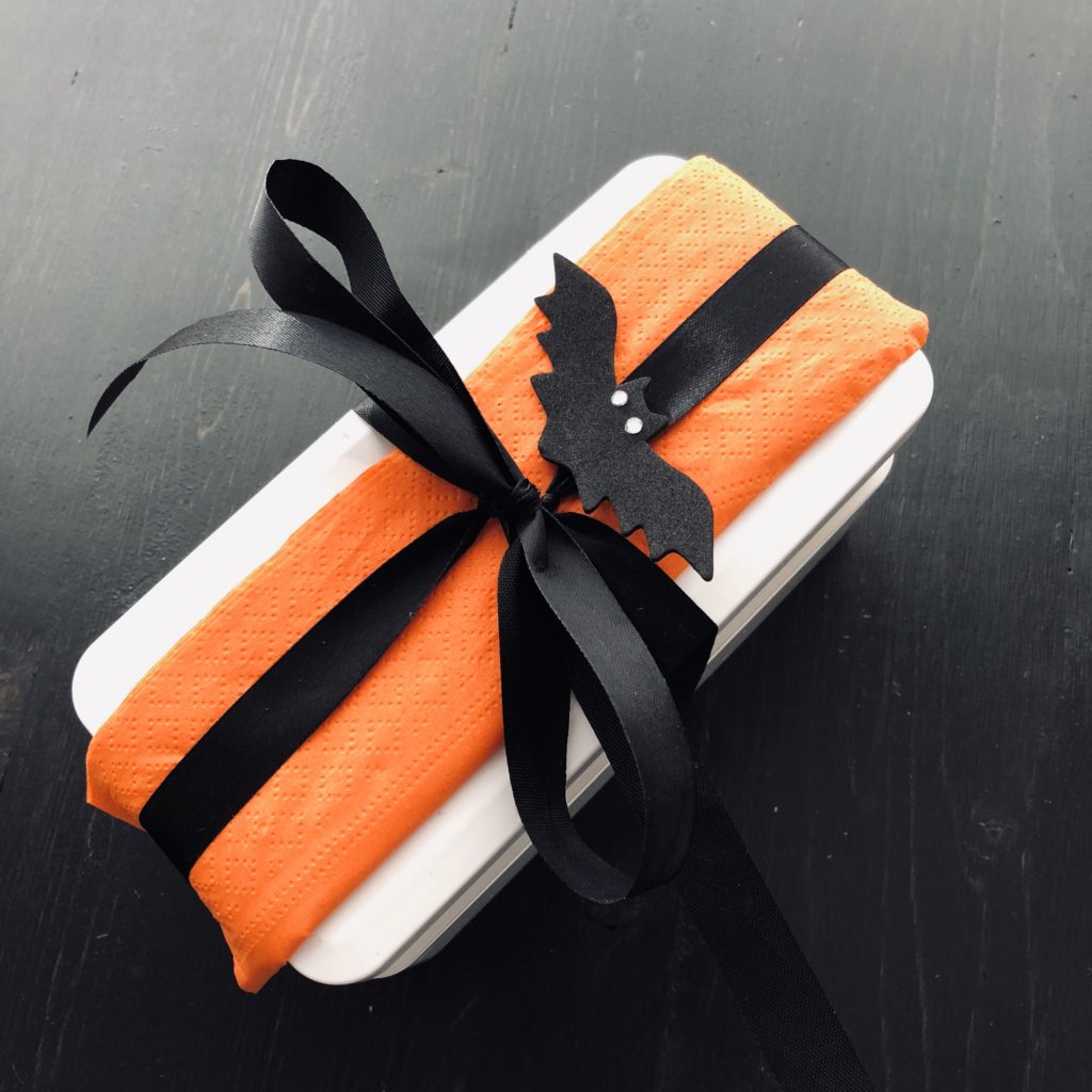 To decorate a Halloween bento box, add an orange napkin, a black ribbon bow, and a small bat.