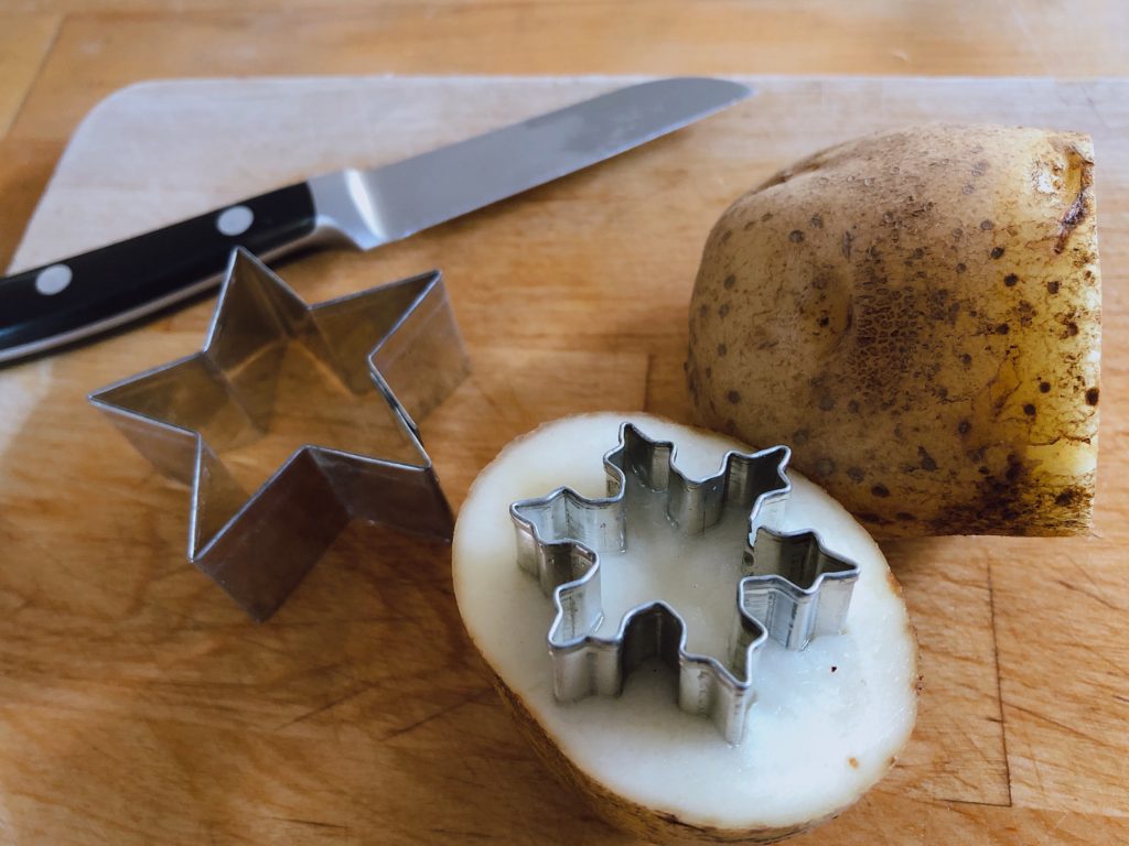 To make a stamp, cut potato and press the sharp end of a metal cookie cutting into the cut side of the potato.
