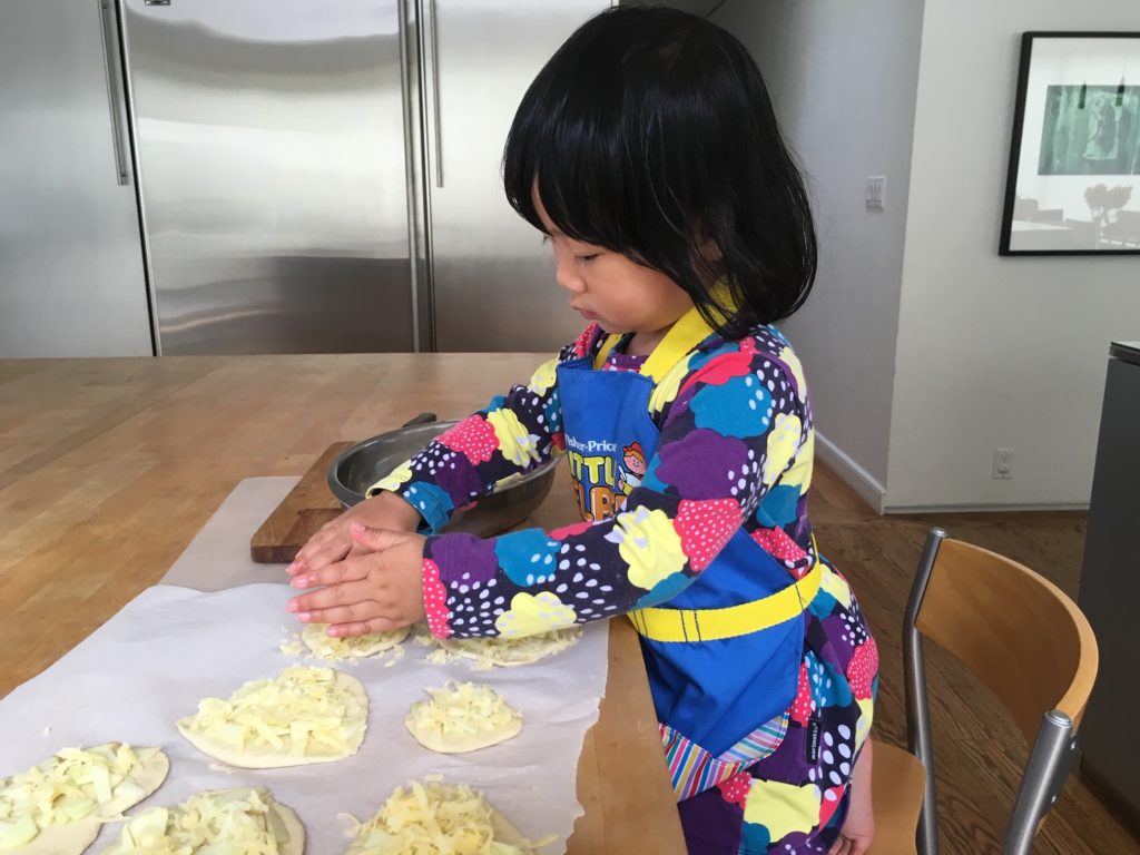 A three-year-old can roll out pizza dough and add toppings.