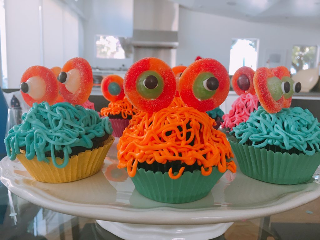 Colorful monster cupcakes arranged on a footed cake plate.