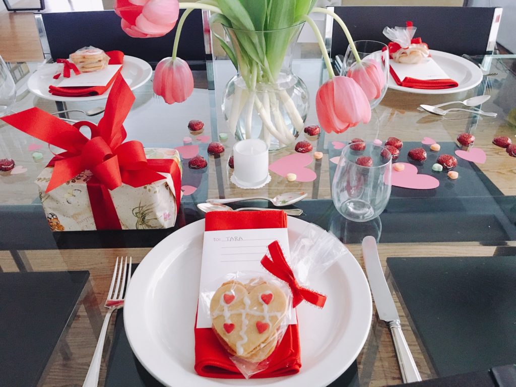 Set each place with a valentine and homemade cookies. Pink tulips, and a scattering of valentine chocolates and paper hearts finish the table decor.