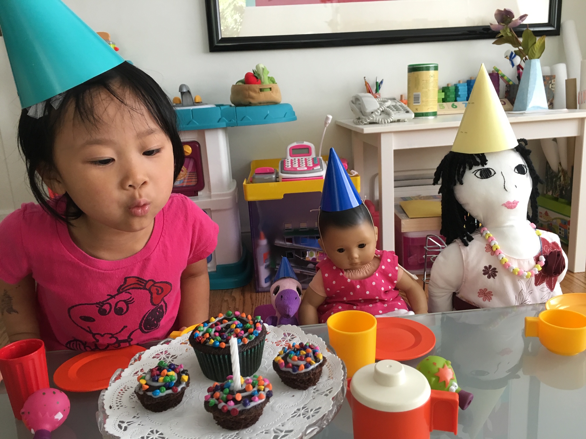 The child blows out the candle for the doll at her doll party.