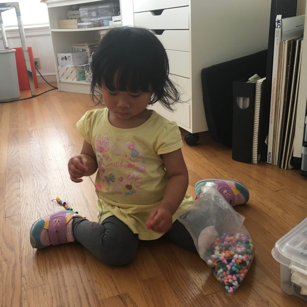 Stringing beads to make necklaces as gifts for her dolls.