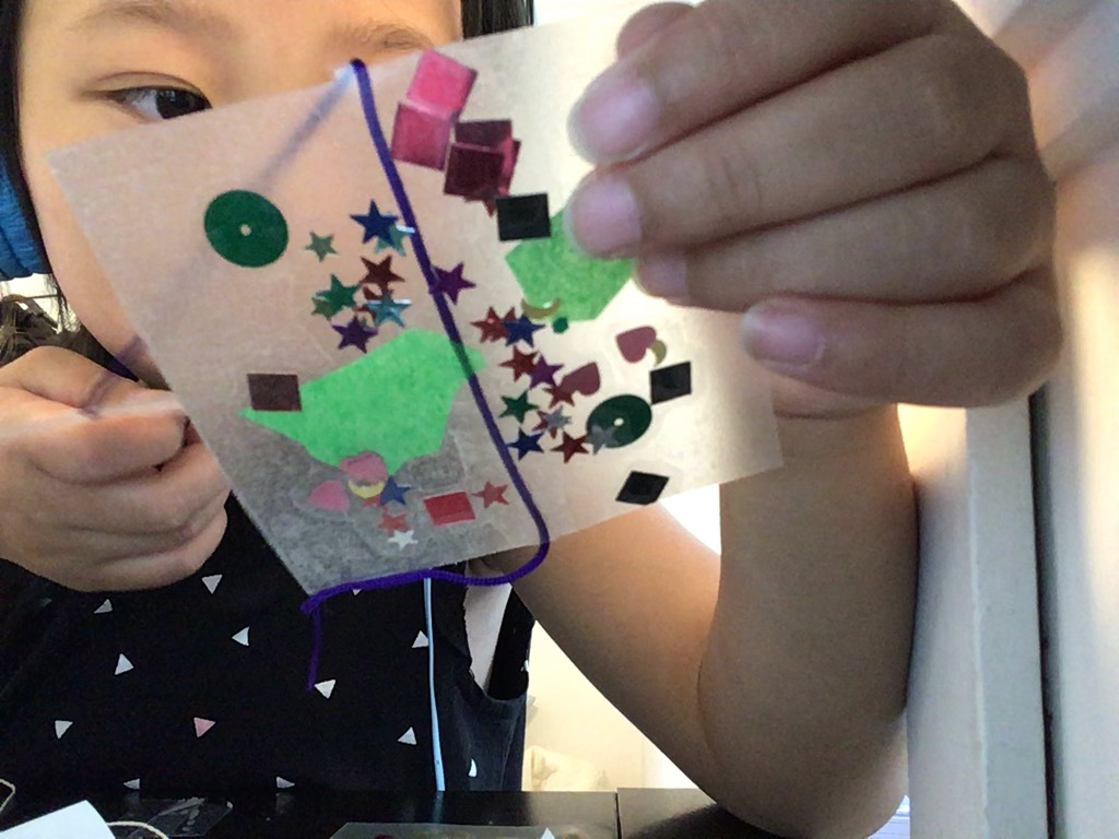 A child examines her first art square made with sequins, tissue paper and confetti.