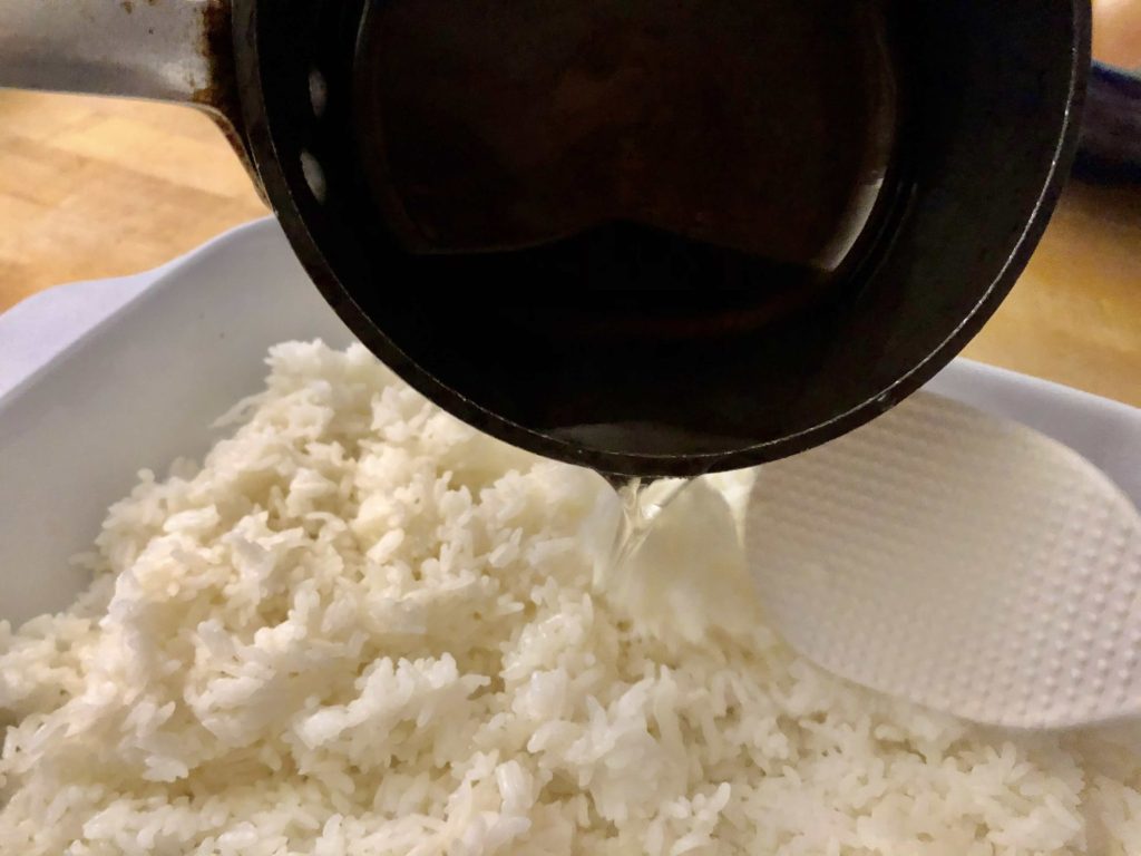 To make sushi at home, start with hot cooked rice, add the vinegar sauce, and toss with a rice paddle to incorporate.