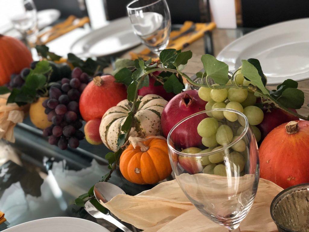 The Thanksgiving table set with pumpkins, squashes, grapes, ivy, and pomegranates.