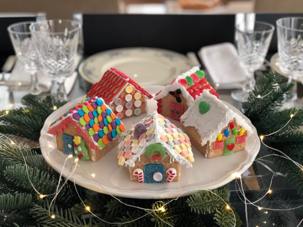 "Gingerbread" houses made from graham crackers are arranged on a cake plate and used as a simple Christmas centerpiece, along with greens and micro lights.
