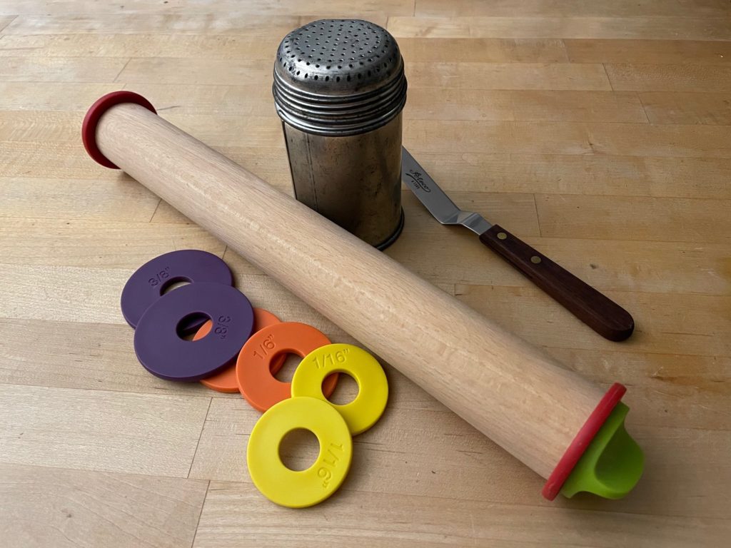 Cookie baking tools that help kids with baking: adjustable rolling pin, powdered sugar shaker for flour, and a small offset spatula.
