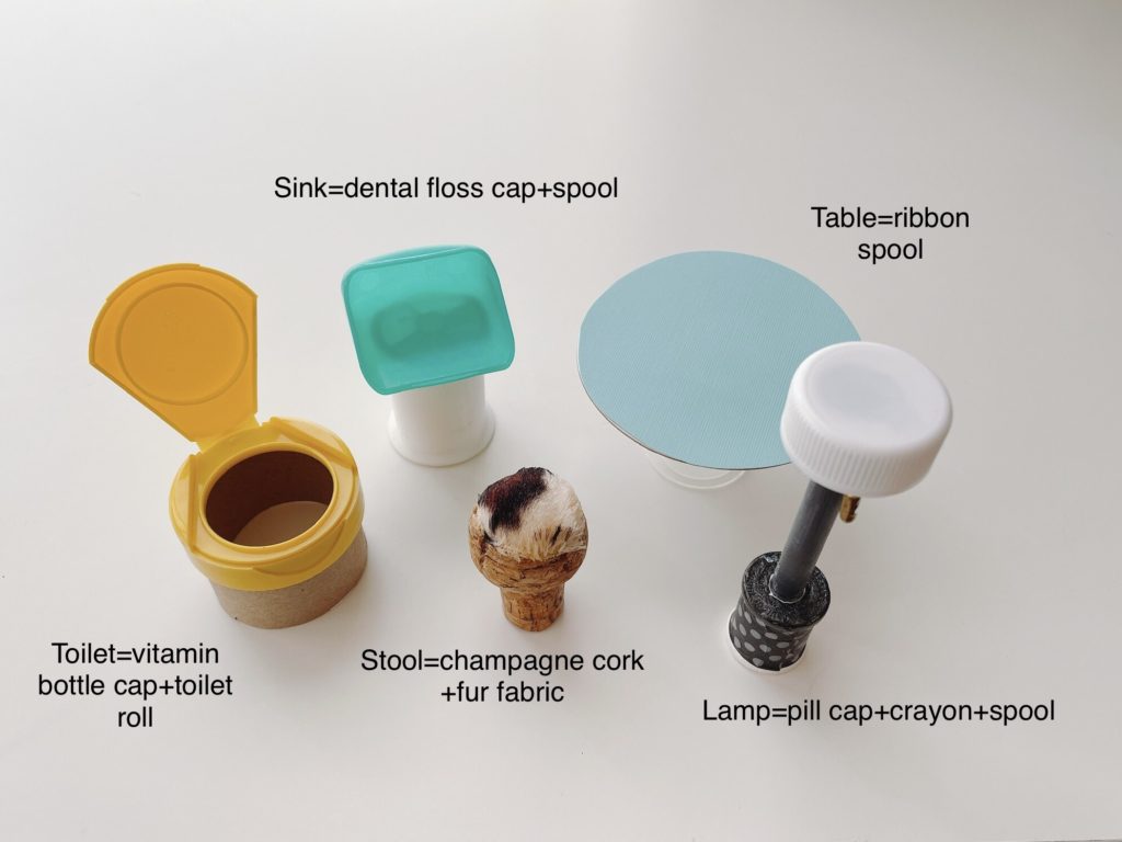 Various odds and ends, such as an empty thread spool, flip-top vitamin jar, and dental floss cap are used to make furniture for a shoebox dollhouse.