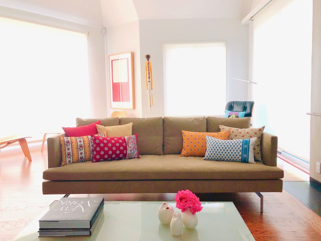 Colorful, home-sewn pillows with. French fabrics and geraniums in a vase add cheer to the home.