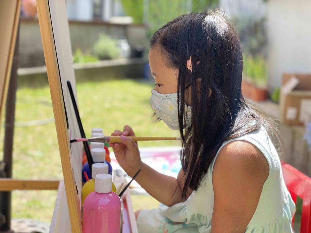 A seven-year-old child paints at an easel outdoors, getting fresh air, while expressing her creativity.