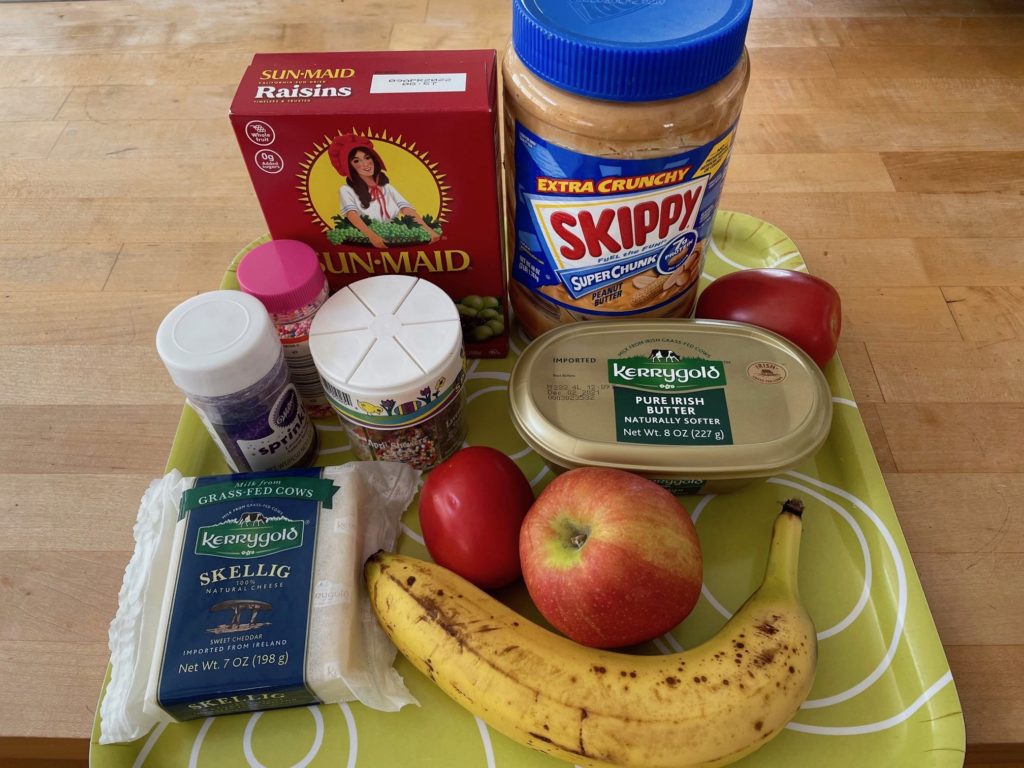 Ingredients for a DIY healthy snack sandwich: raisins peanut butter, fruits and vegetables, cheese, butter, and cookie sprinkles just for fun.