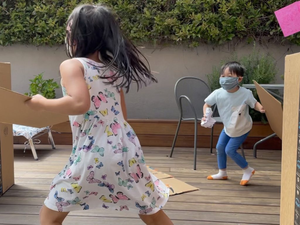 The children play fort fight using cardboard cartons as forts and crumpled recycled paper for ammunition.