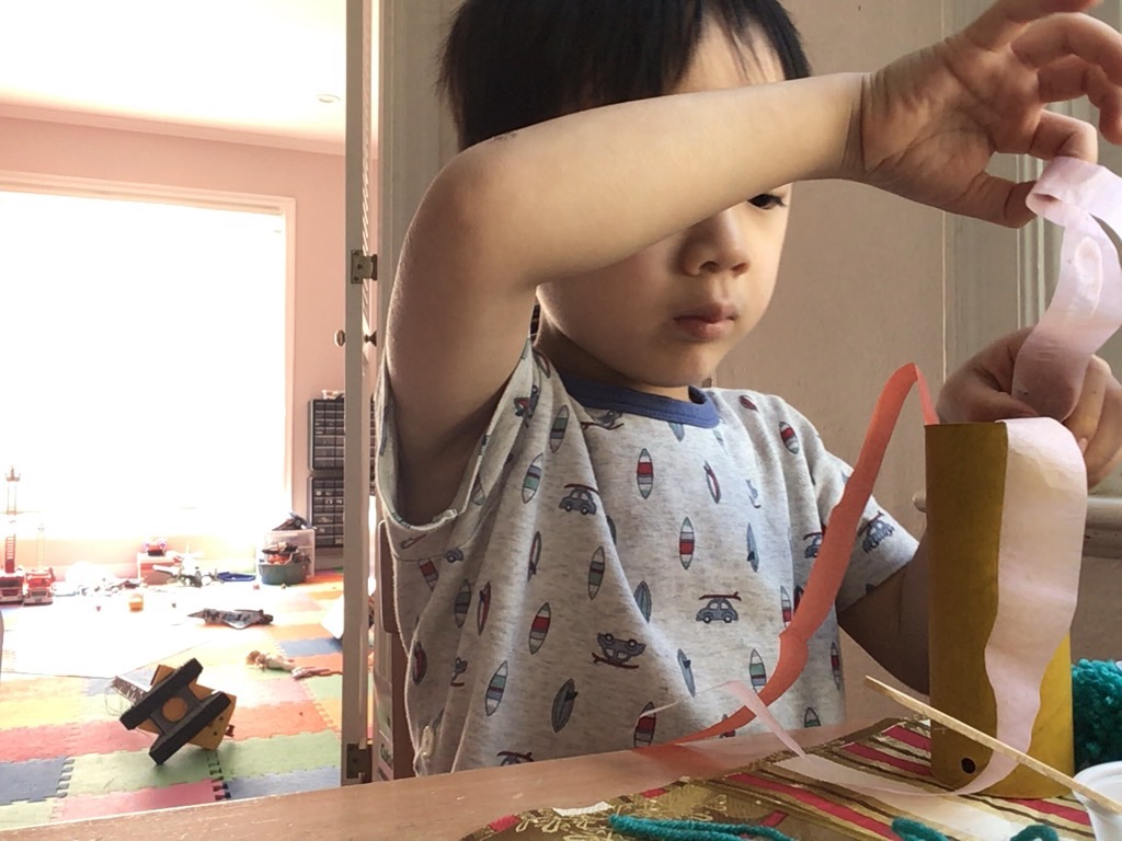 The grandchild follows instructions from grandma, long distance, to make a fire-breathing dragon with tissue paper, a toilet paper roll, and pom poms.