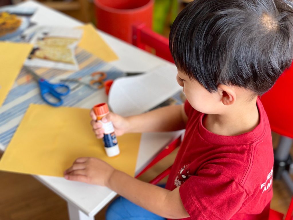 Child glues down cut-out images onto printer paper in preparation for making a book.