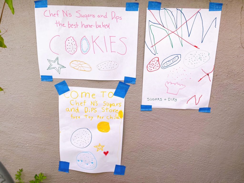 Hand-drawn posters taped to the garden wall promote the cookie shop.