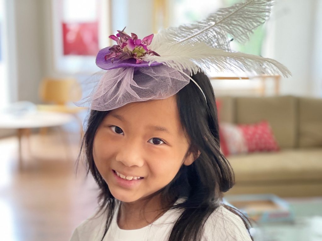 Small fascinator made from a circle of felt with flowers, feathers, and tulle.