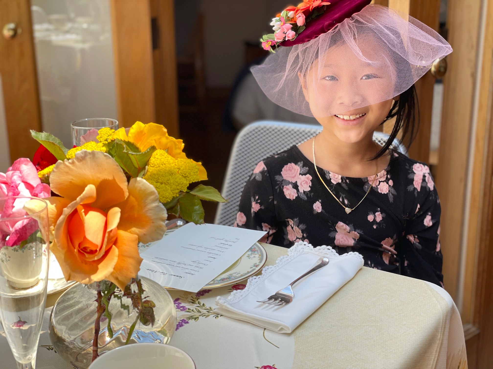 Child in homemade fascinator at table, waiting for a tea party to begin.