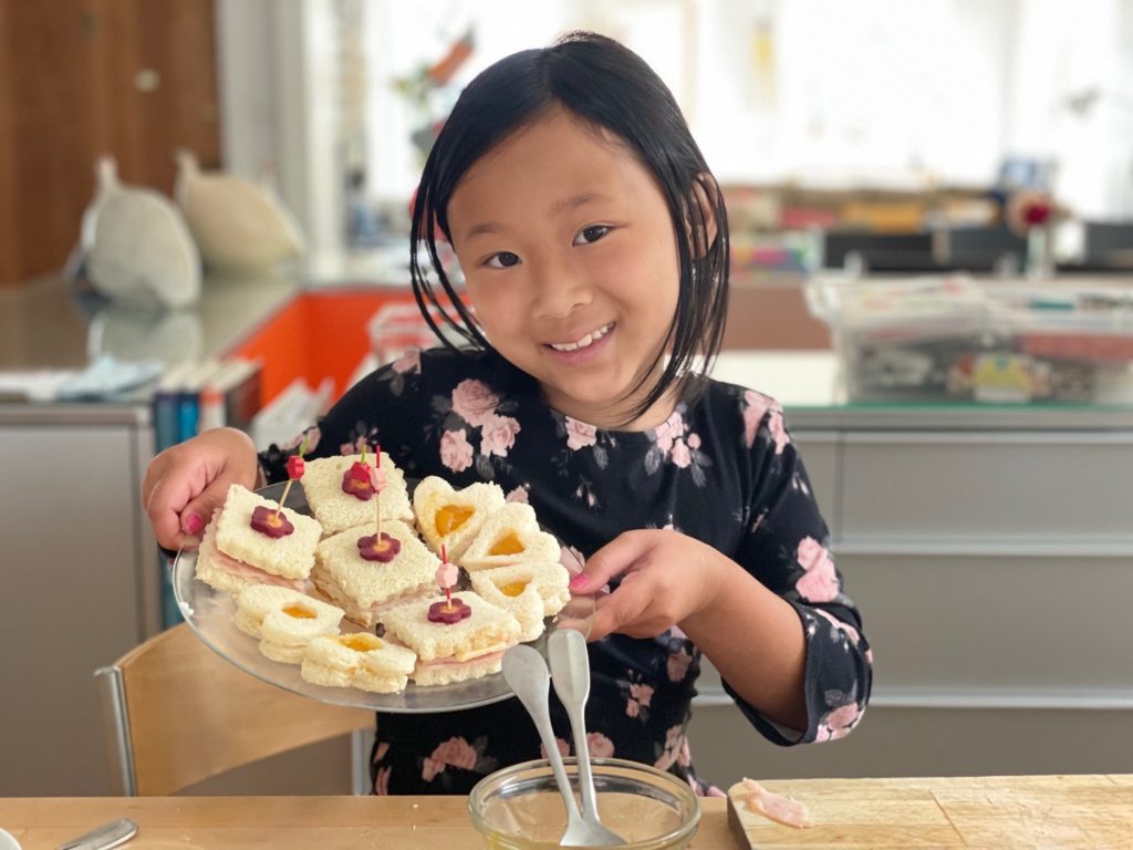 Miss T displays the tea sandwiches she made: jam and cream cheese for one, turkey and cheese for the other.