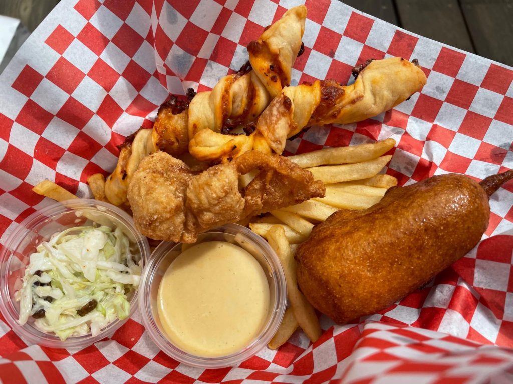 The snacks: pizza sticks, chicken tenders, french fries, corn dogs and coleslaw are served in red plastic fast food baskets with checked paper liners.