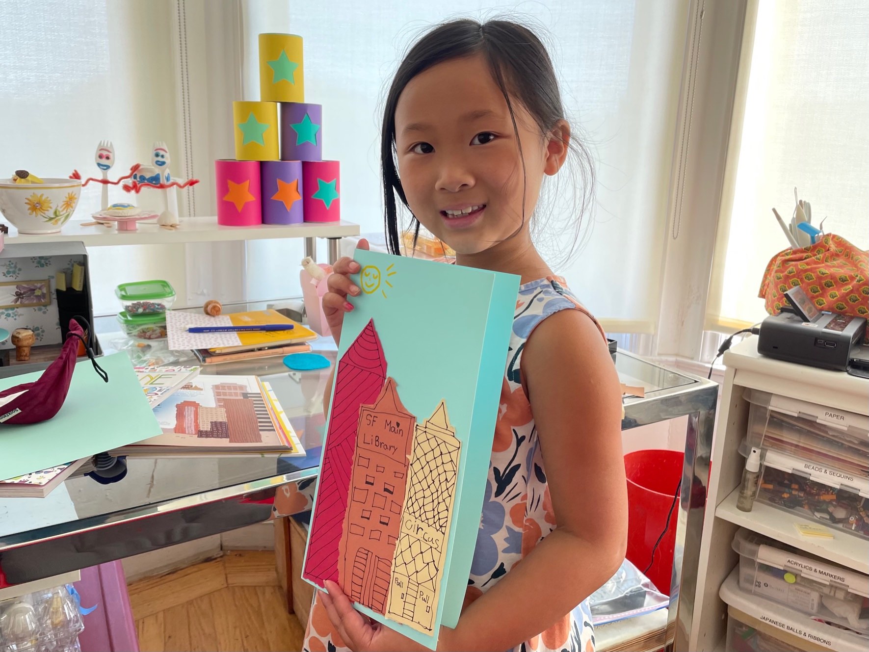 Child shows a cityscape card made with torn paper.