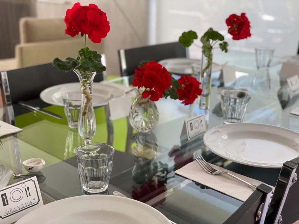 Entertaining is part of grandma life. For a casual table setting for a Friday night family dinner, the centerpiece is geraniums cut from an indoor houseplant and arranged in glass vases. 