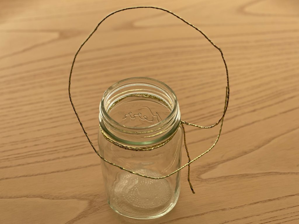 To make a fairy lantern, first loop wire around the neck of a mason jar and make a handle.
