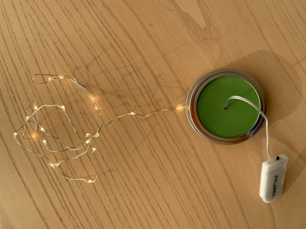 To string lights for the fairy lantern, replace the inner lid of a mason jar with a cardboard circle, bore a hole through the cardboard, and thread the light string through.
