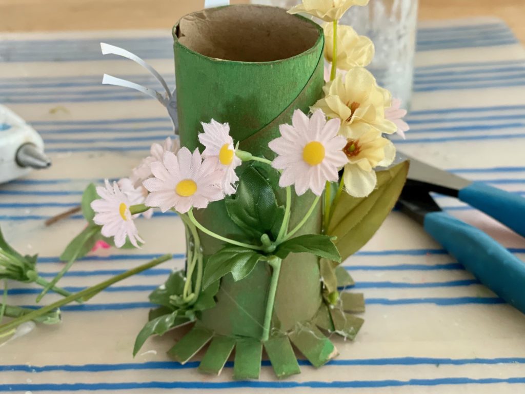 Paint a toilet roll green, snip the bottom and splay the snips for stability; hot glue flowers and stems for the back of the fairy lantern.