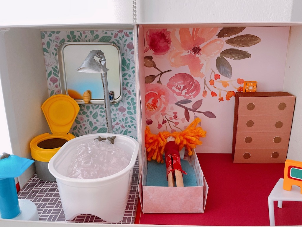 The bathroom features a tub from a Pringles container and a toilet from a Kirkland calcium bottle container. The chest of drawers in the bedroom is a small box.