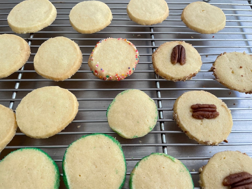 Cookies cooling on a rack. This butter cookie recipe offers variations: some are edged in sprinkles, others feature colored sugar, and chopped nuts.