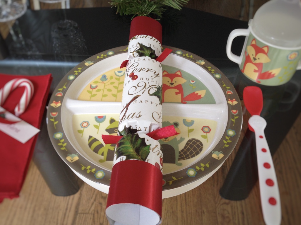 A toddler's table setting for a special dinner. The child's everyday, non-breakable plates is dressed up with a Christmas cracker and candy cane place card.