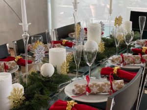 Table setting with candles and snowflakes for height, pine branches and red napkins for color.