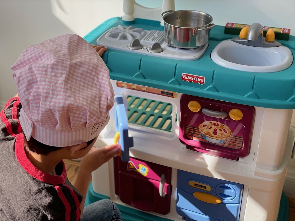Child in front of the toy stove, playing the restaurant game.