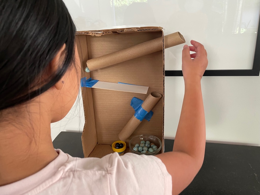 Adjust the tubes and runway strips and keep testing with marbles until the track you make enables the marble to travel down to the bottom of the box.