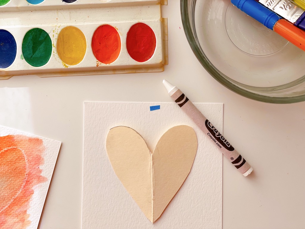 DIY valentines start by tracing a heart shape with a white crayon, then painting over with watercolors to bring out the heart design.