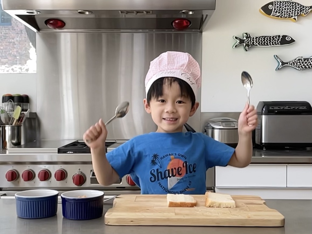 Child demonstrating how to make a peanut butter and jelly sandwich as a pretend TV cooking star.