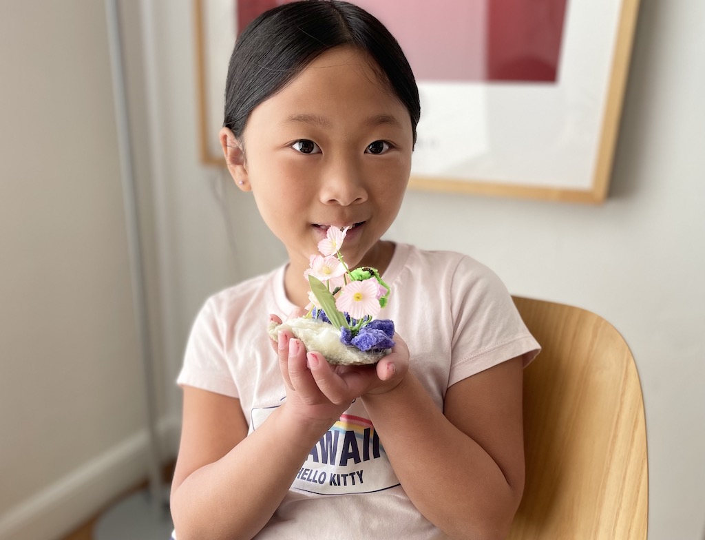 Child and her original floral creation made from discarded foam bits, artificial flowers, and a pipe cleaner palm tree.
