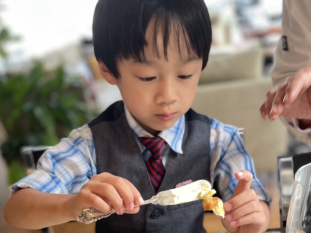 Learning dining etiquette for kids: child butters his dinner roll with his butter knife.