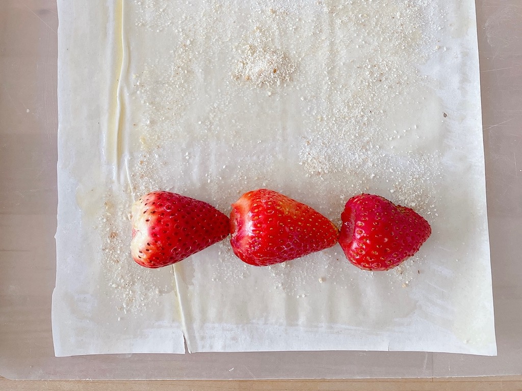 Step 1: brush phyllo sheet with butter, sprinkle with breadcrumb-sugar mixture, and line up hulled berries to get ready for rolling.