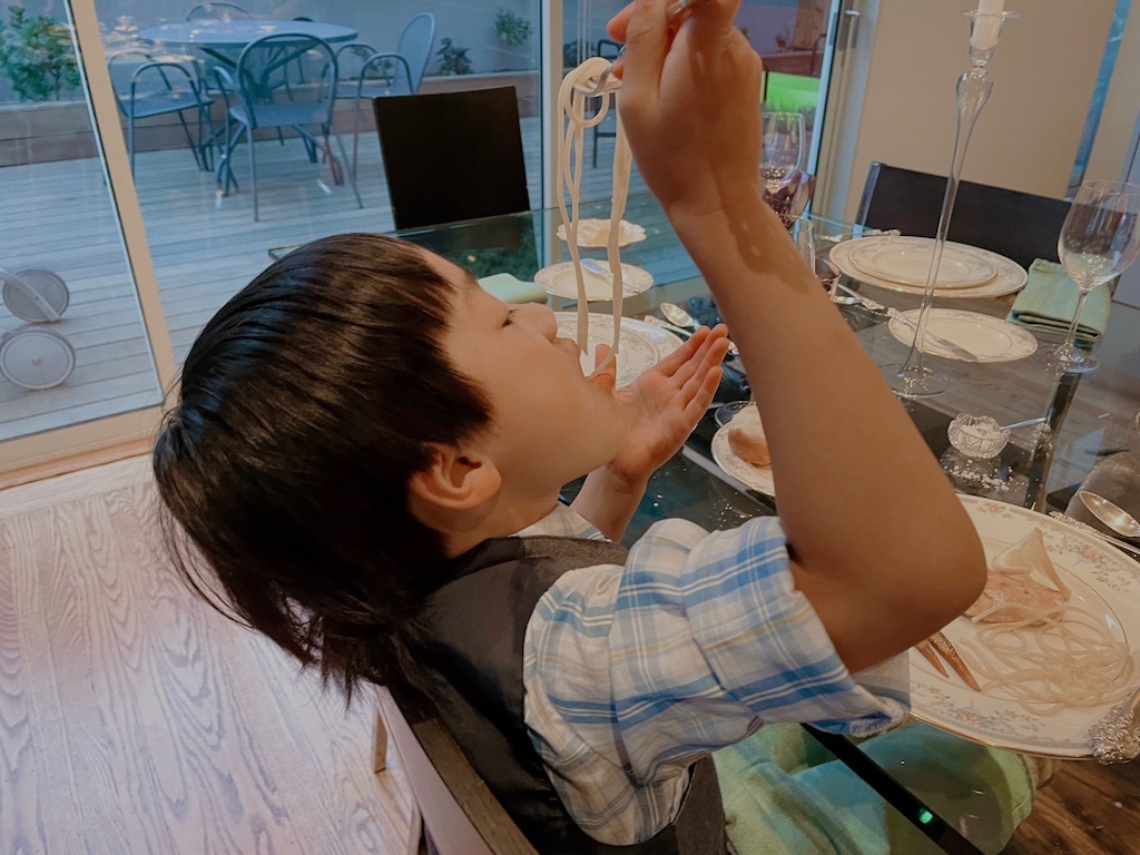 Child dangling spaghetti over his mouth, a breach for good dining etiquette, but a chance to have some fun.