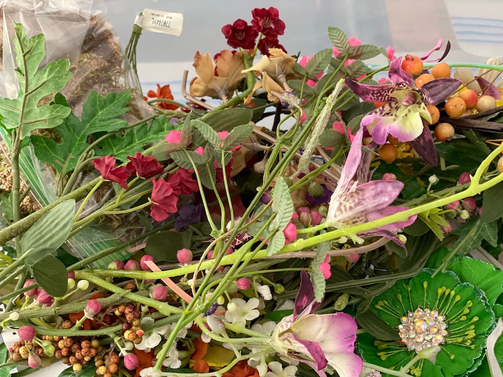 A plastic bin full of artificial flowers can be incorporated into the notebook collage design.