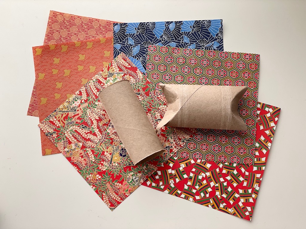 A selection of origami papers show the possibilities for decorating a toilet paper roll as a gift box for a Mother's Day video on a flash drive.