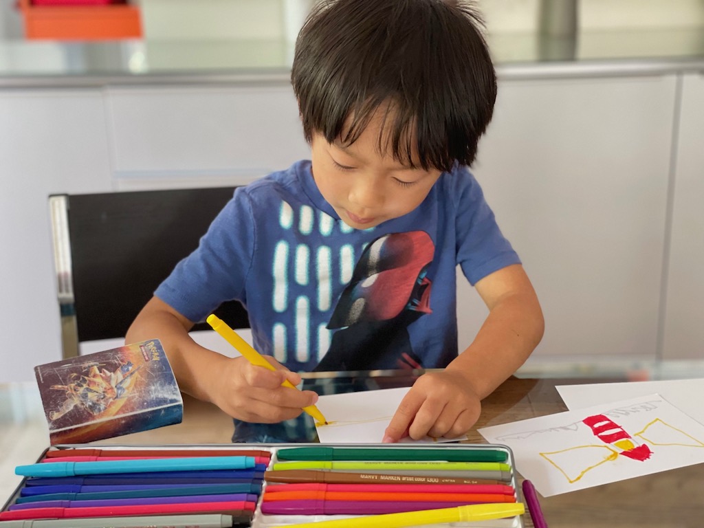 Child draws the flag of Sweden. Next to him is a lighthouse postcard that he drew after watching a Swedish travelogue.