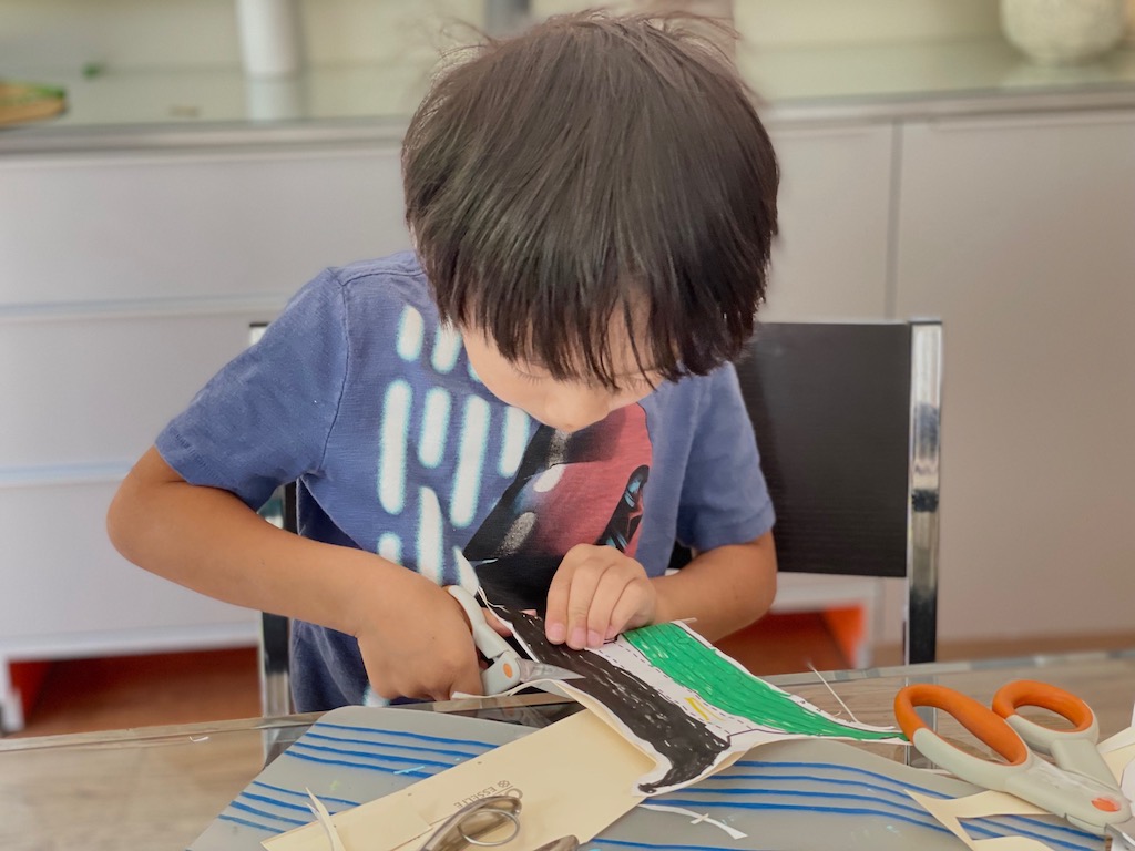 Child cuts out elements to make a Viking ship as part of the pretend travel experience.