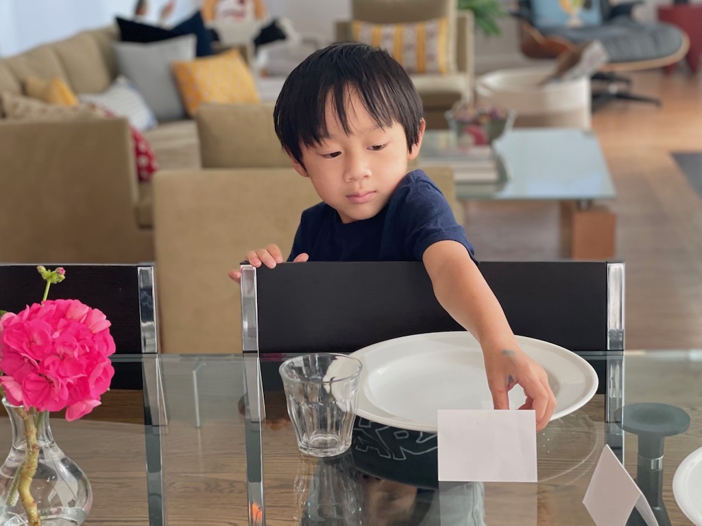 A five-year-old sets the table for dinner. The one who sets the table gets to decide where everyone sits. Place cards mark the places.